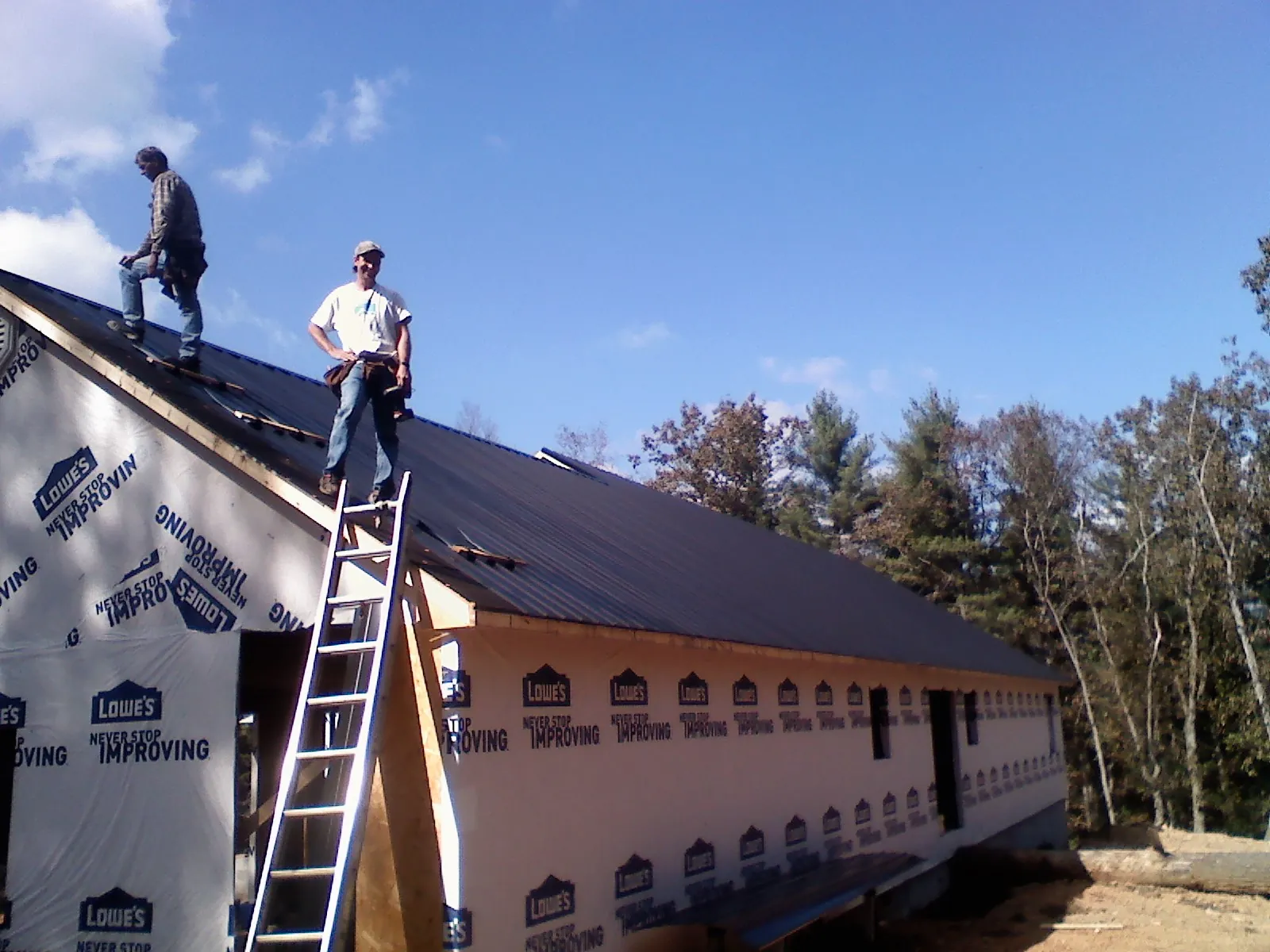 Two roofers standing on a long dark metal roof over a wrapped building in Toledo